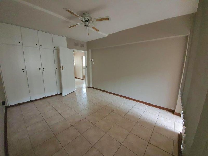 A spacious, empty bedroom featuring neutral tiled flooring, built-in cupboards for storage, and a ceiling fan, offering a blank canvas for personalization.