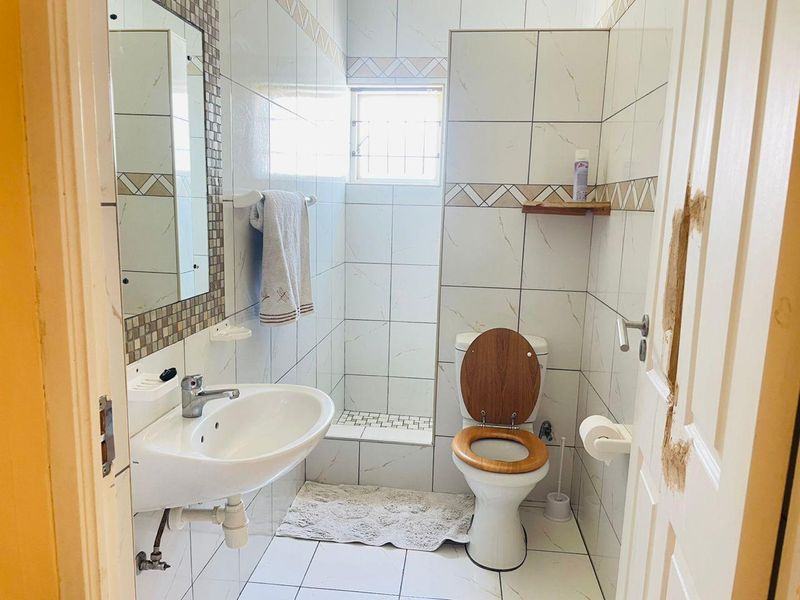 A functional bathroom featuring tiled walls and flooring, a pedestal basin, a toilet, and a tiled shower enclosure.