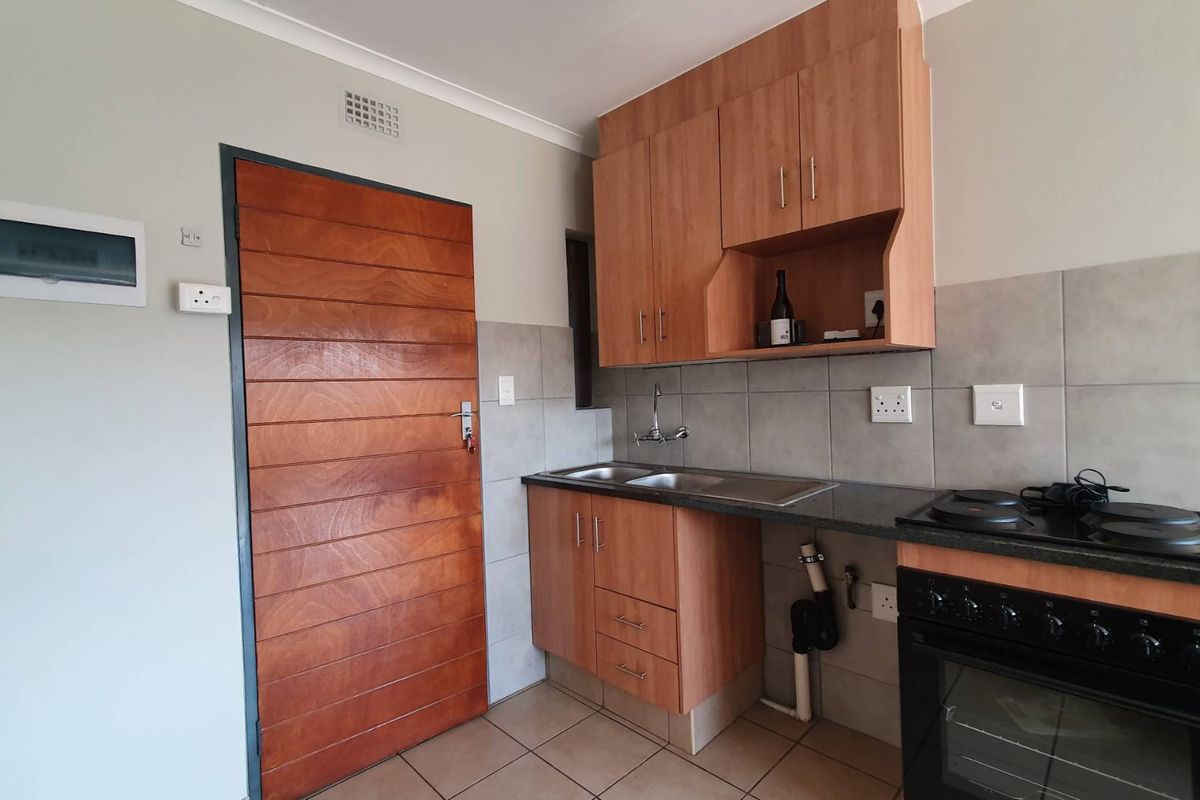 A compact kitchen featuring wooden cabinetry, a tiled backsplash, built-in oven and stove, and tiled flooring.