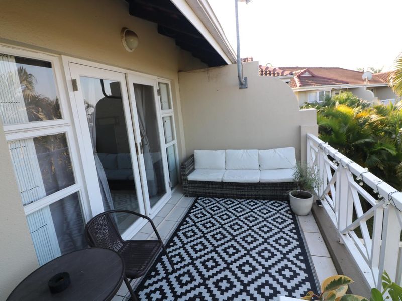 A covered balcony featuring tiled flooring, a white wooden balustrade, and sliding glass door access to the interior living space.