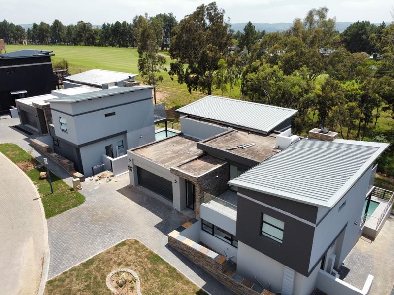 Aerial view of a modern multi-level residential property featuring contemporary architectural design, stone cladding, metal roofing, and a paved driveway.