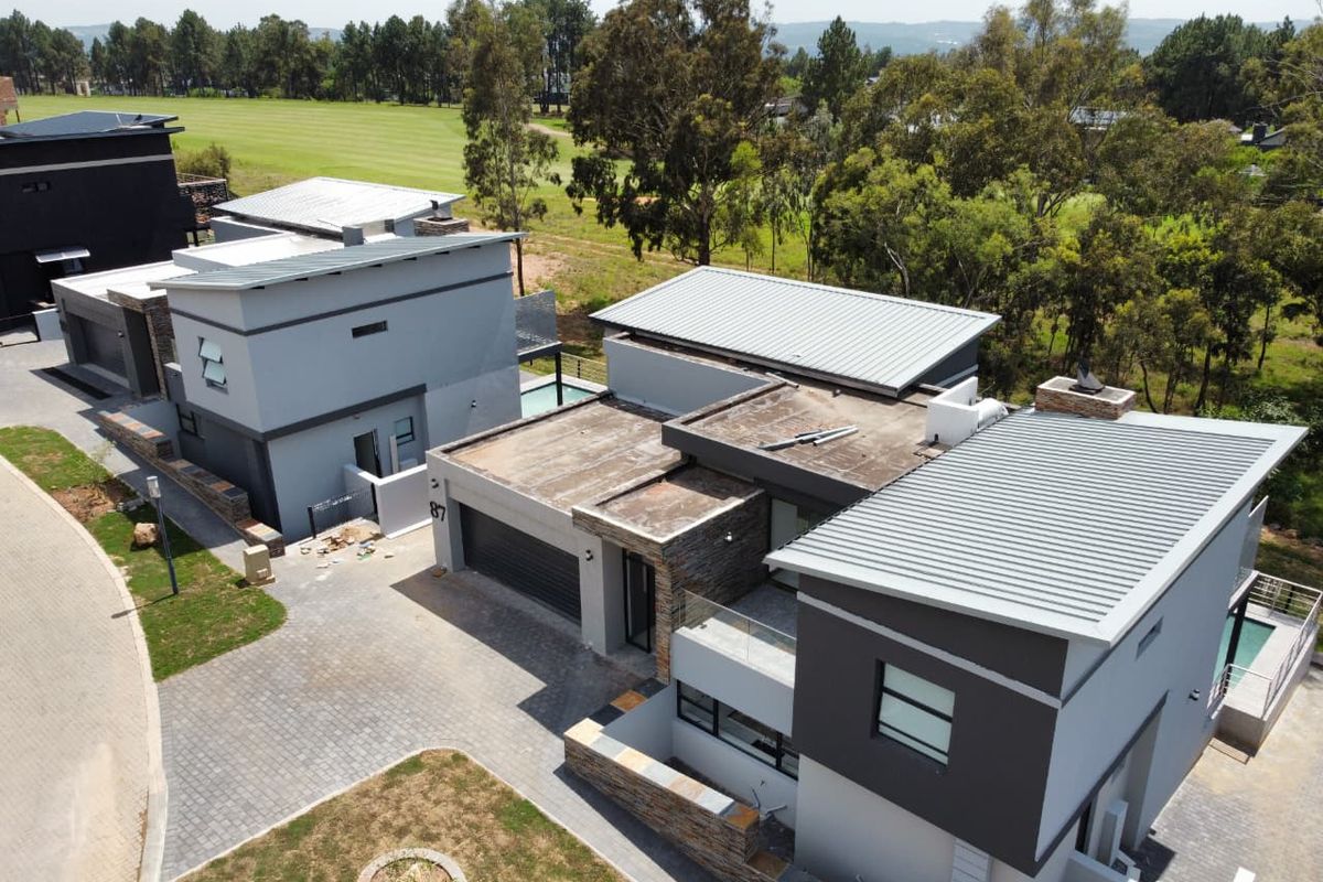 Aerial view of a modern multi-level residential property featuring contemporary architectural design, stone cladding, metal roofing, and a paved driveway.