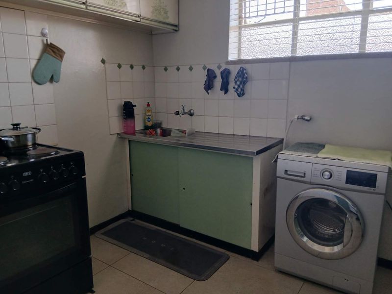 A functional kitchen area featuring a stainless steel sink, tiled splashback, and built-in cabinetry, offering potential for modernization and aesthetic updates.