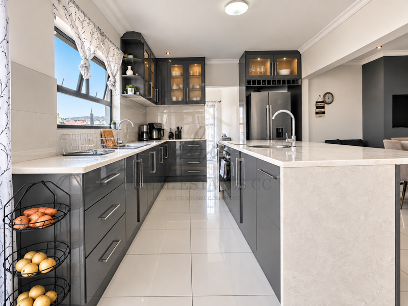 Modern kitchen featuring sleek dark grey cabinetry, white quartz countertops, a central island with a sink, and polished tiled flooring.