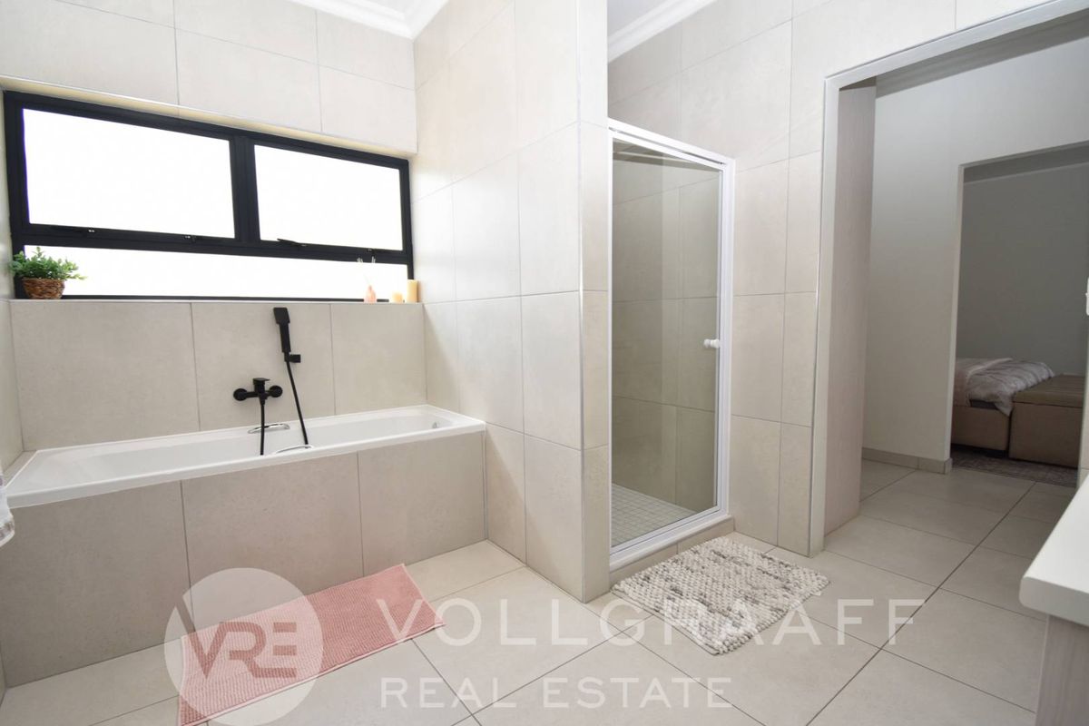 Modern bathroom featuring a built-in bathtub with black tapware, a separate shower enclosure, and neutral floor-to-ceiling tiling.
