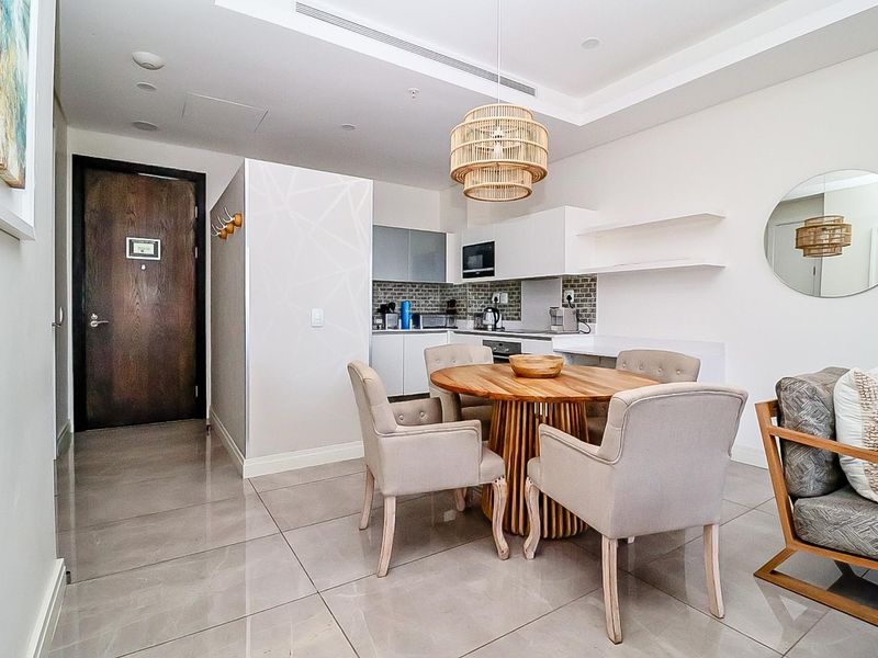 Modern open-plan living and kitchen area featuring sleek cabinetry, stone countertops, tiled flooring, and integrated appliances in a well-maintained apartment setting.