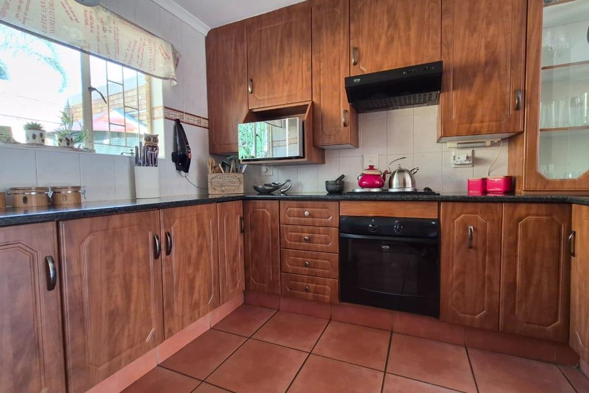 A functional kitchen featuring traditional wood-finish cabinetry, dark granite countertops, built-in oven, extractor fan, and terracotta floor tiles.