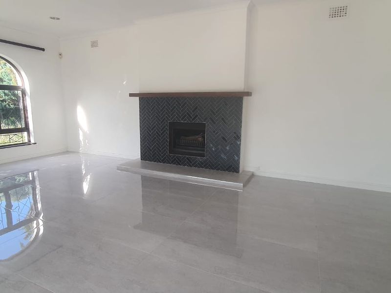Spacious living room featuring polished tile flooring, an arched window, and a modern fireplace with a striking herringbone tile surround.