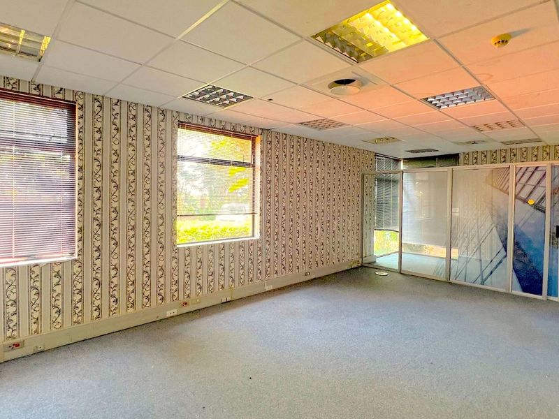 An empty office space featuring a suspended ceiling, recessed lighting, large windows with blinds, and a glass partition wall.