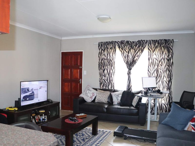 A functional living room featuring tiled flooring, a solid wooden door, and coved ceilings, providing a comfortable and practical living space.