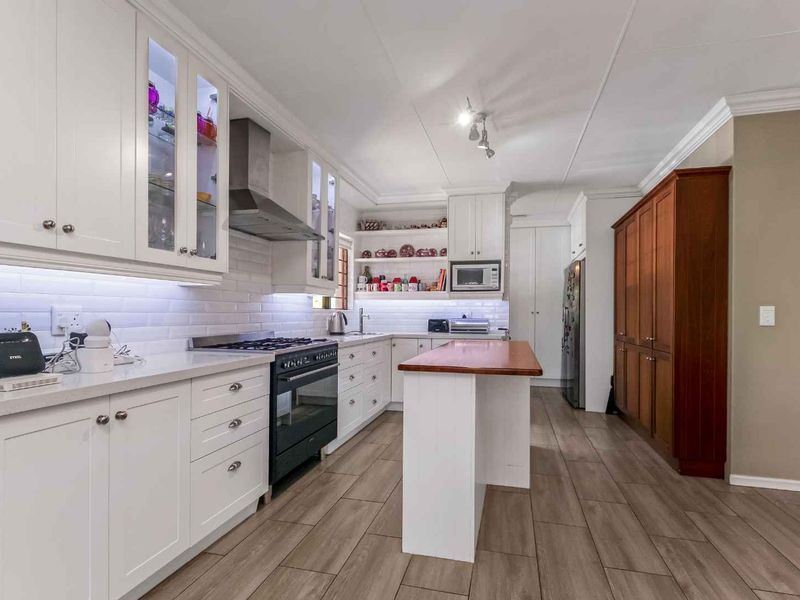 Modern kitchen featuring white shaker cabinetry, subway tile backsplash, quartz countertops, a central wooden island, and high-quality wood-look tile flooring.