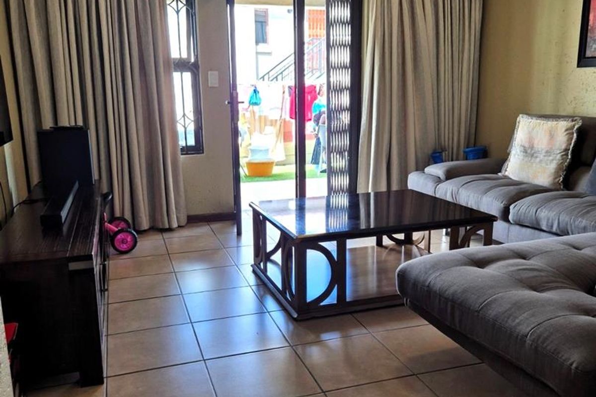 A living room featuring tiled flooring and a sliding glass door with a security gate, providing access to an outdoor area.