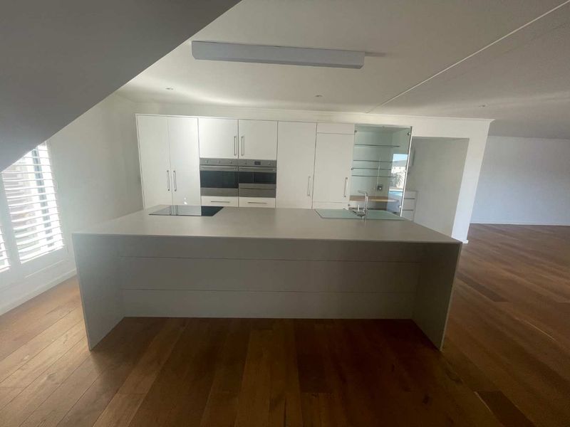 Modern kitchen featuring a large central island, integrated double ovens, induction cooktop, and sleek white cabinetry set against warm hardwood flooring.
