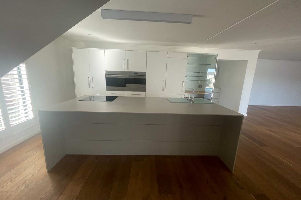 Modern kitchen featuring a large central island, integrated double ovens, induction cooktop, and sleek white cabinetry set against warm hardwood flooring.