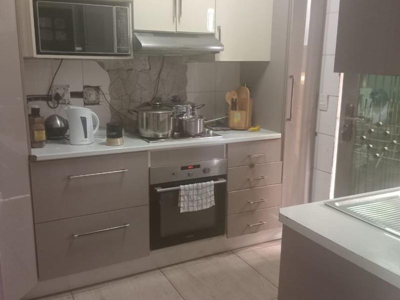 Compact kitchen featuring modern laminate cabinetry, built-in oven, extractor fan, and tiled flooring, with a functional layout and stone countertops.