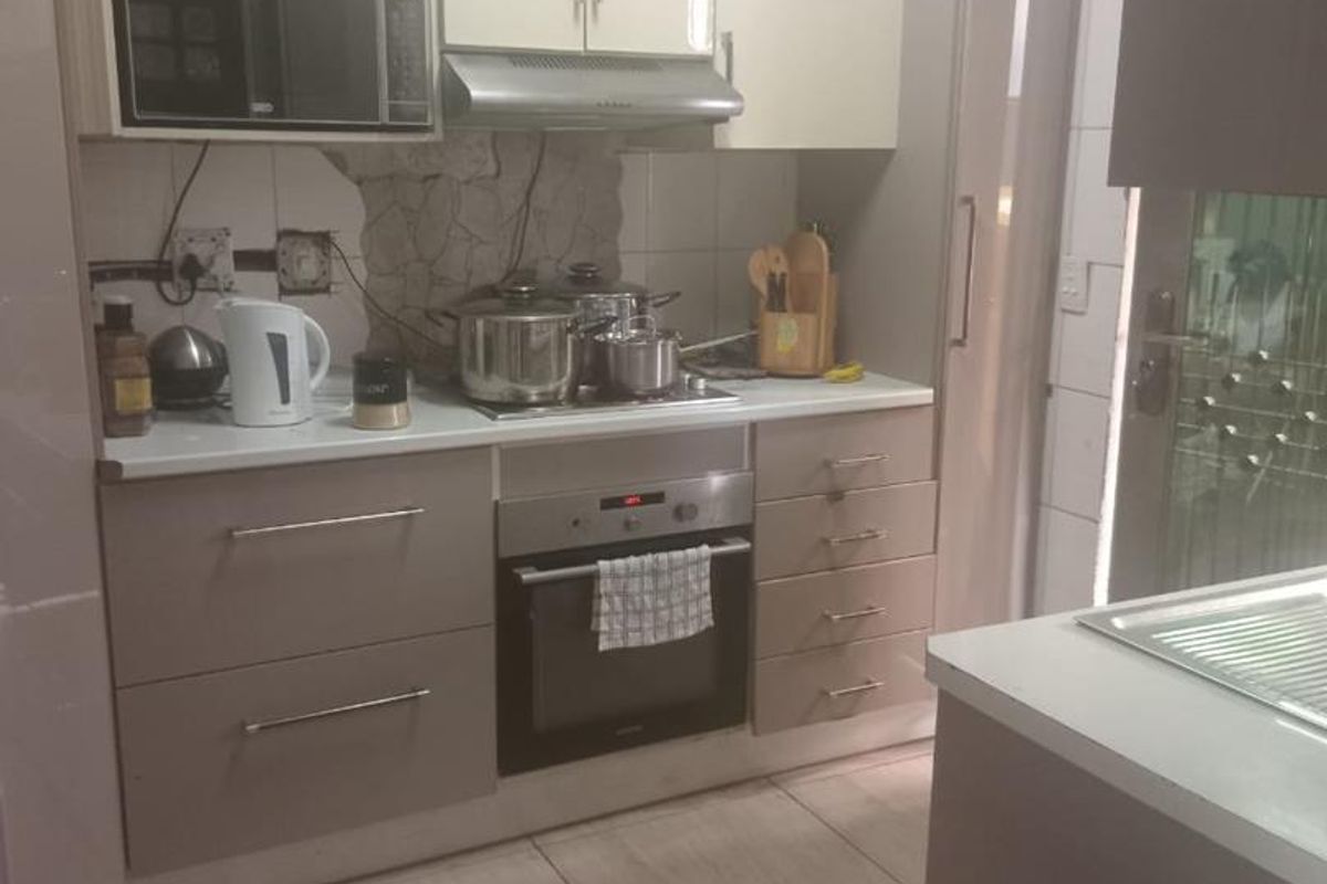 Compact kitchen featuring modern laminate cabinetry, built-in oven, extractor fan, and tiled flooring, with a functional layout and stone countertops.