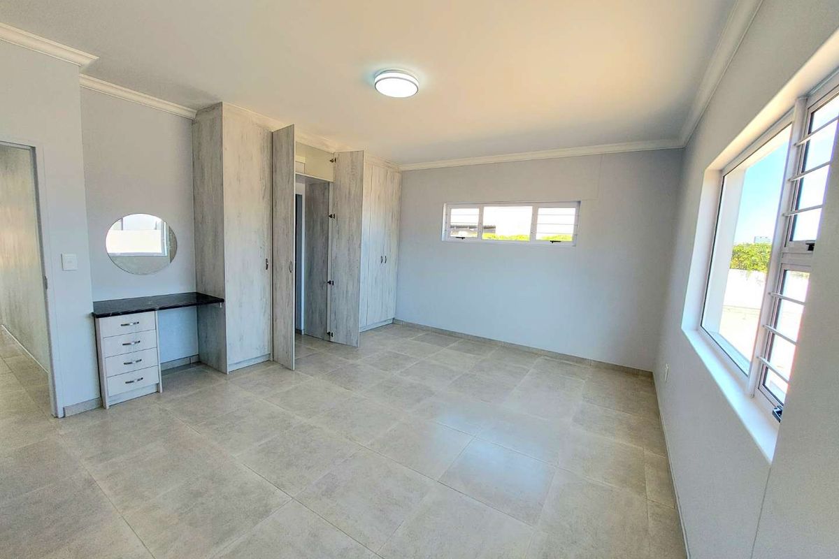 A bright, spacious bedroom featuring neutral floor tiles, built-in cupboards with a vanity area, and large windows providing ample natural light.