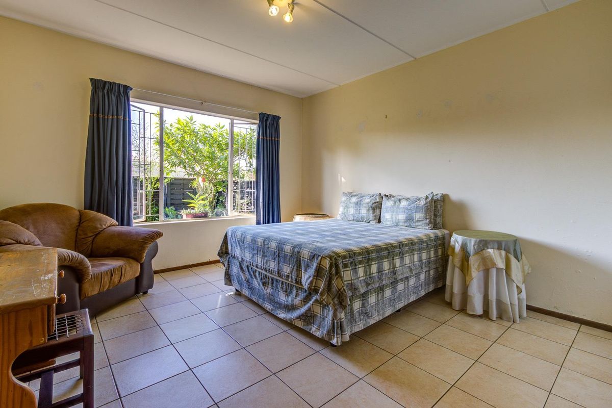 A spacious bedroom featuring neutral tiled flooring, large windows providing natural light, and a functional layout suitable for various furniture arrangements.