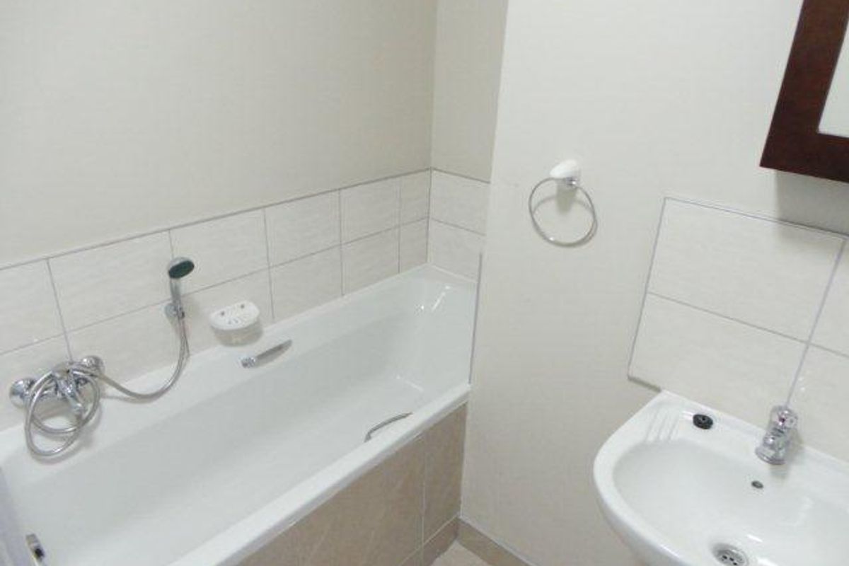 A functional bathroom featuring a white bathtub with a handheld shower attachment and a wall-mounted basin with chrome fixtures.
