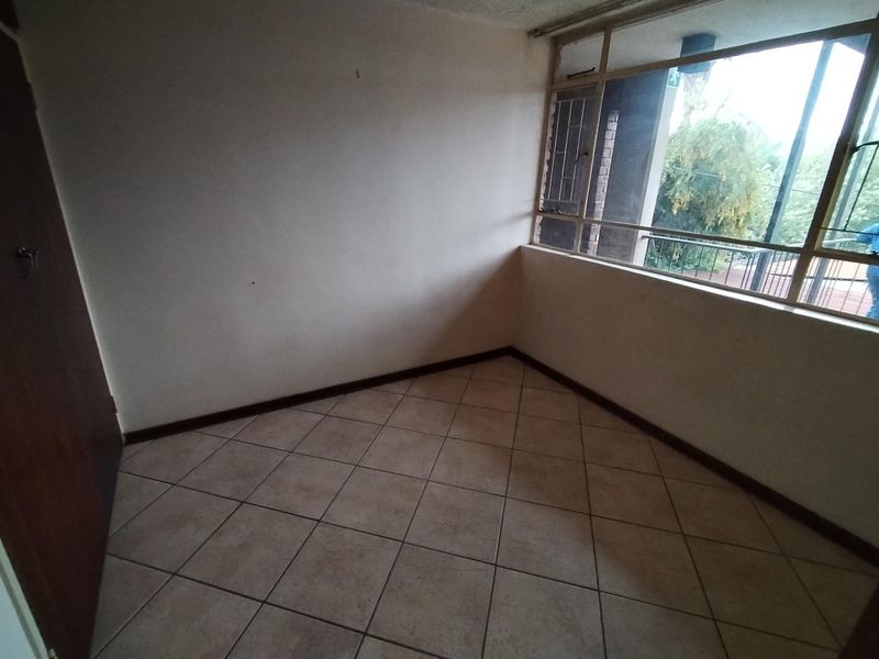 An empty bedroom featuring tiled flooring and a large window, providing a blank canvas for potential interior design and renovation.