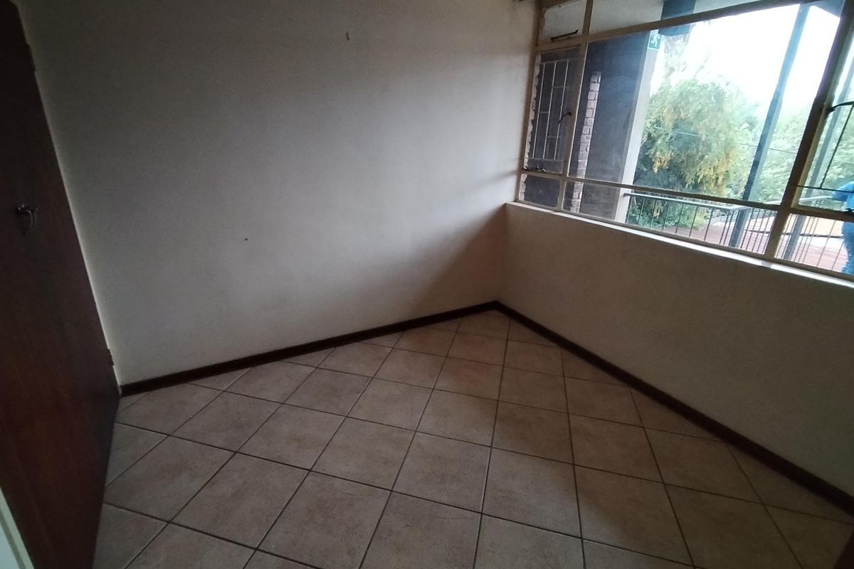 An empty bedroom featuring tiled flooring and a large window, providing a blank canvas for potential interior design and renovation.
