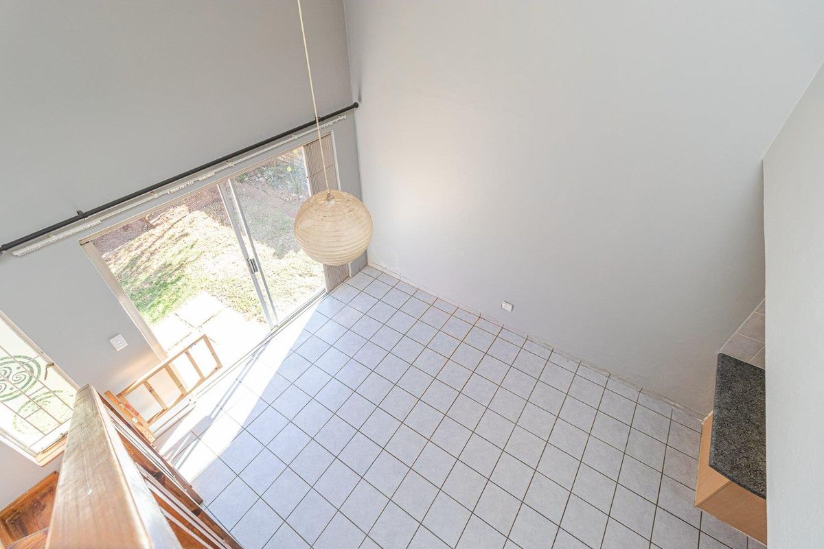 High-ceiling living area featuring tiled flooring, a large sliding glass door providing natural light, and direct access to the outdoor space.