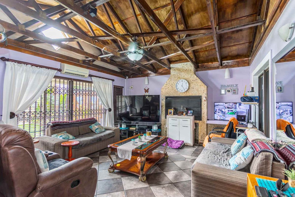 Spacious living room featuring a vaulted timber-beamed ceiling, tiled flooring, and a built-in fireplace with stone-cladding detail.