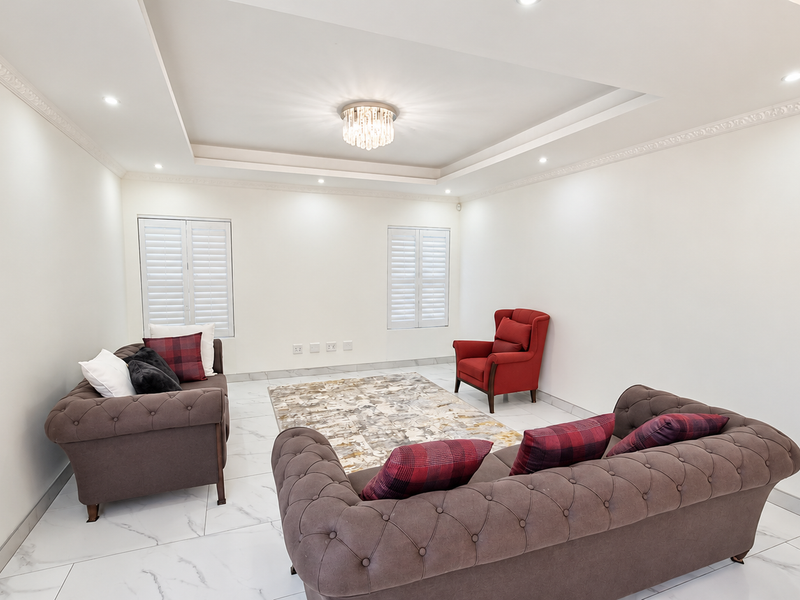 Spacious living room featuring elegant marble-look flooring, a recessed ceiling with crown molding, and plantation shutters, creating a bright and sophisticated atmosphere.