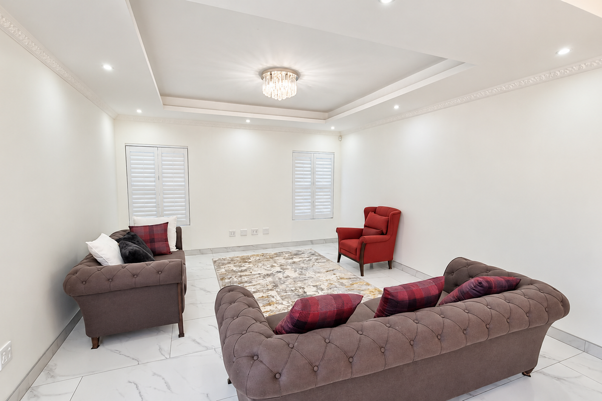 Spacious living room featuring elegant marble-look flooring, a recessed ceiling with crown molding, and plantation shutters, creating a bright and sophisticated atmosphere.