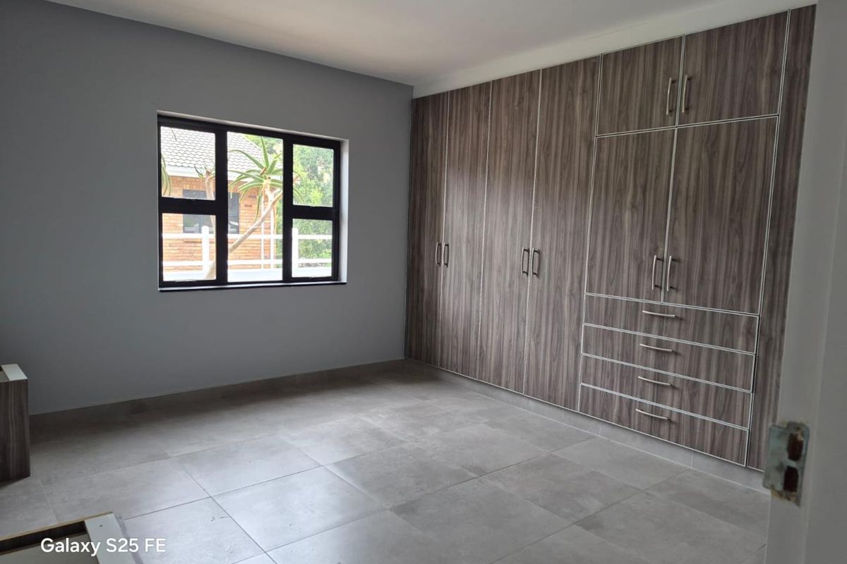A spacious, empty bedroom featuring modern grey floor tiles, neutral wall paint, and extensive built-in wooden cabinetry for ample storage.