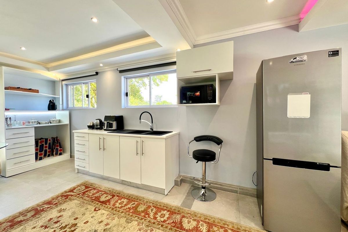 A modern kitchen area featuring white cabinetry, a black sink with a gooseneck faucet, recessed lighting, and tiled flooring.