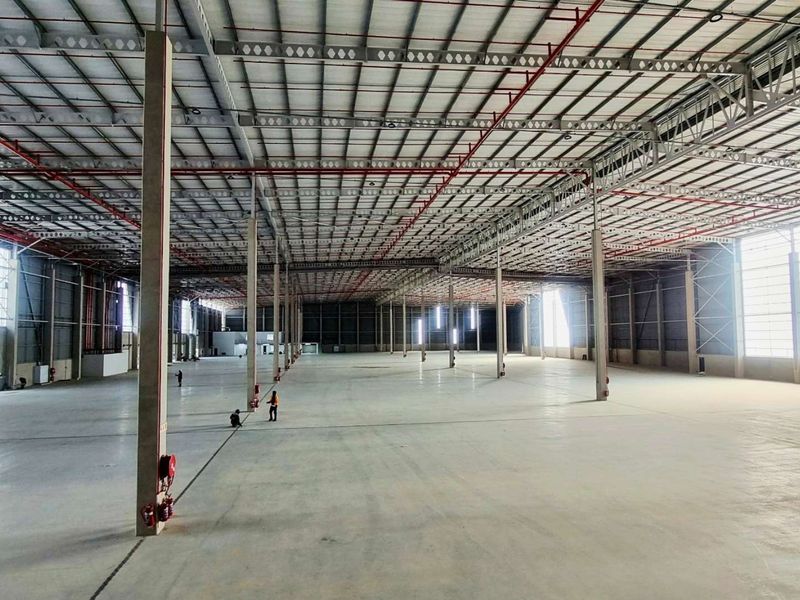 Expansive industrial warehouse space featuring high ceilings with exposed steel trusses, fire sprinkler systems, polished concrete flooring, and large roller shutter access doors.