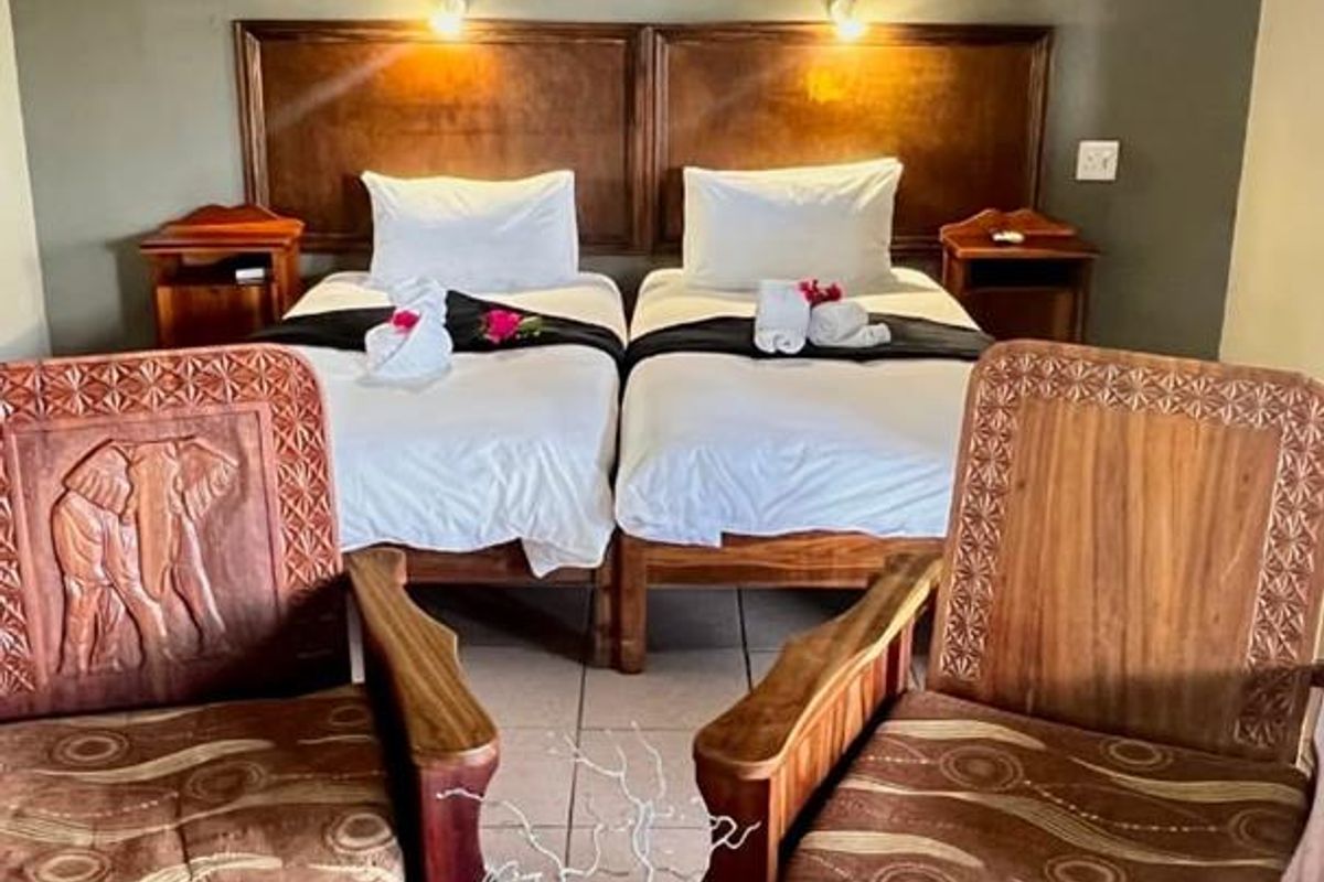 A rustic hotel bedroom featuring a thatched roof, built-in wooden headboards, wall-mounted air conditioning unit, and tiled flooring.