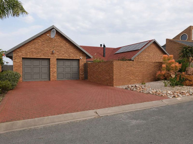 Front view of a brick house featuring a double garage, paved driveway, and roof-mounted solar panels.