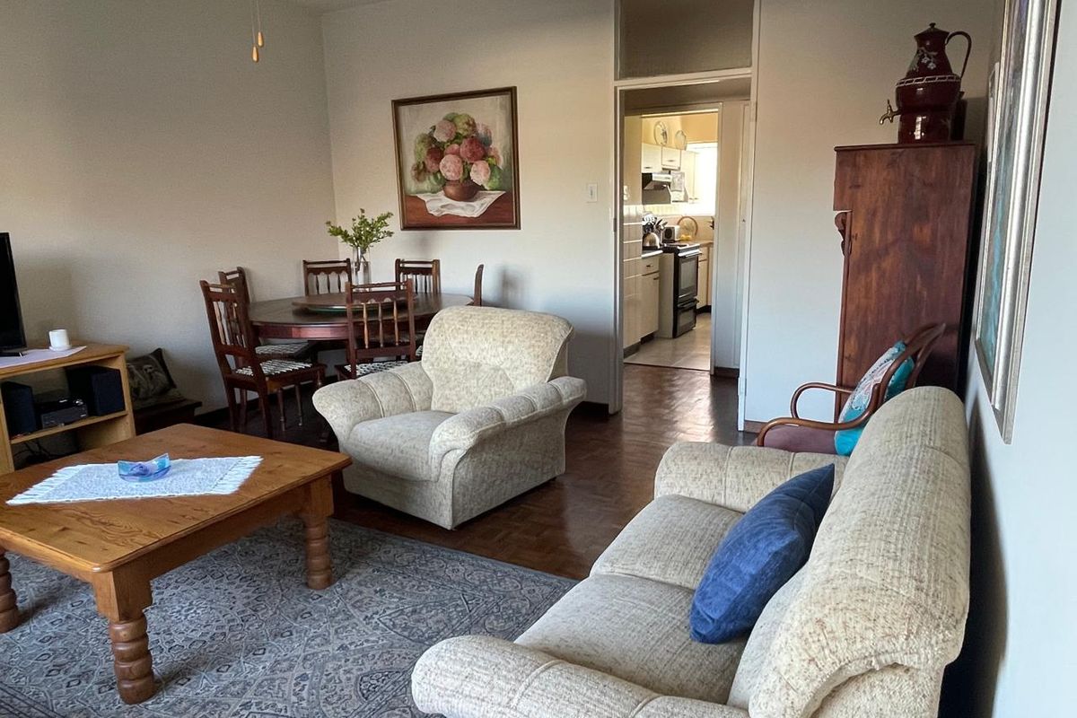 A spacious living and dining area with parquet flooring, leading through to a separate kitchen space.