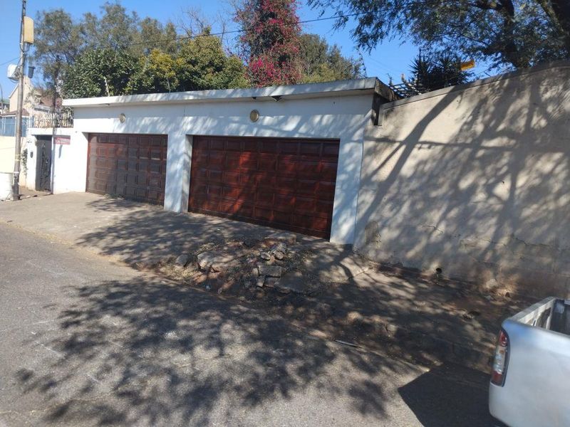 Street-facing double garage with wooden doors and an adjacent perimeter wall showing signs of exterior wear and plaster damage.