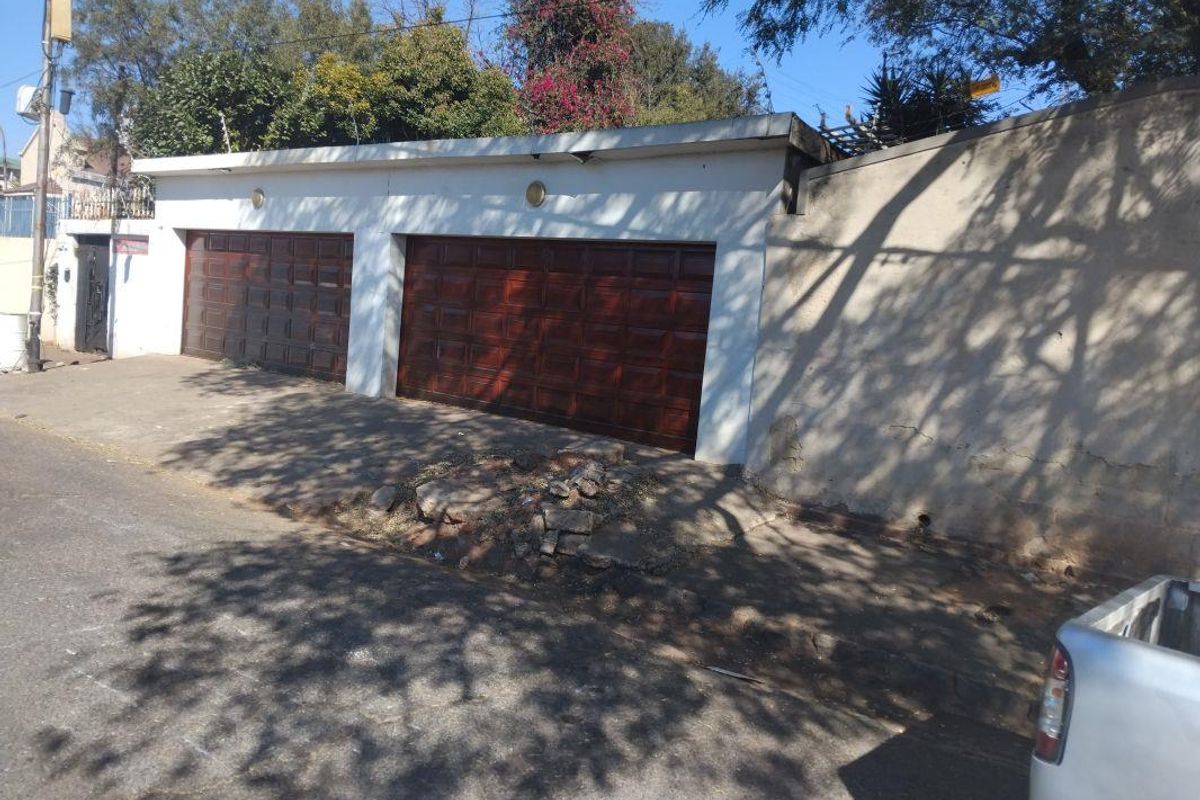 Street-facing double garage with wooden doors and an adjacent perimeter wall showing signs of exterior wear and plaster damage.