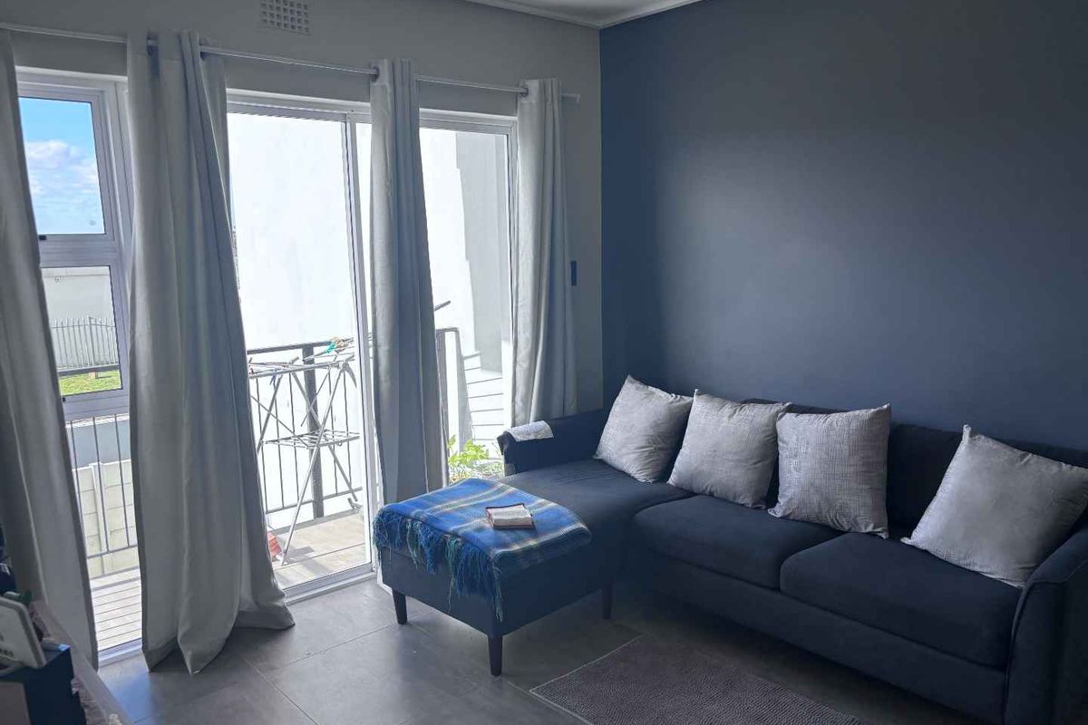 A bright living room featuring large sliding glass doors that open onto a private balcony, complemented by modern tiled flooring and a feature wall.