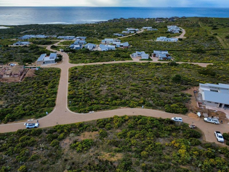 An aerial view of a residential estate featuring paved roads and surrounding coastal vegetation with ocean views in the distance.