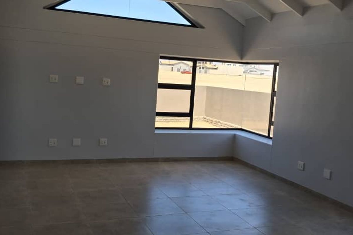 Spacious, light-filled living area featuring high vaulted ceilings, large windows, and neutral tiled flooring, offering a clean and modern blank canvas.
