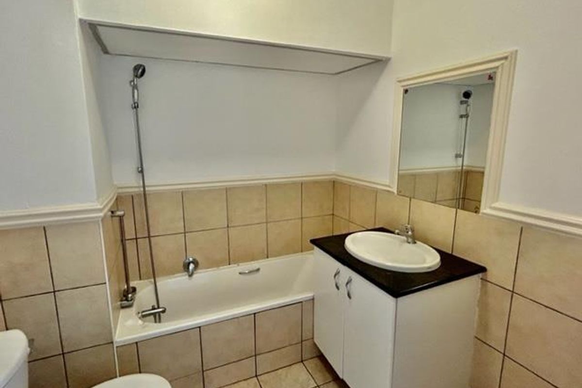 A functional bathroom featuring a built-in bathtub with shower attachment, a vanity cabinet with a basin, and wall-mounted mirror.