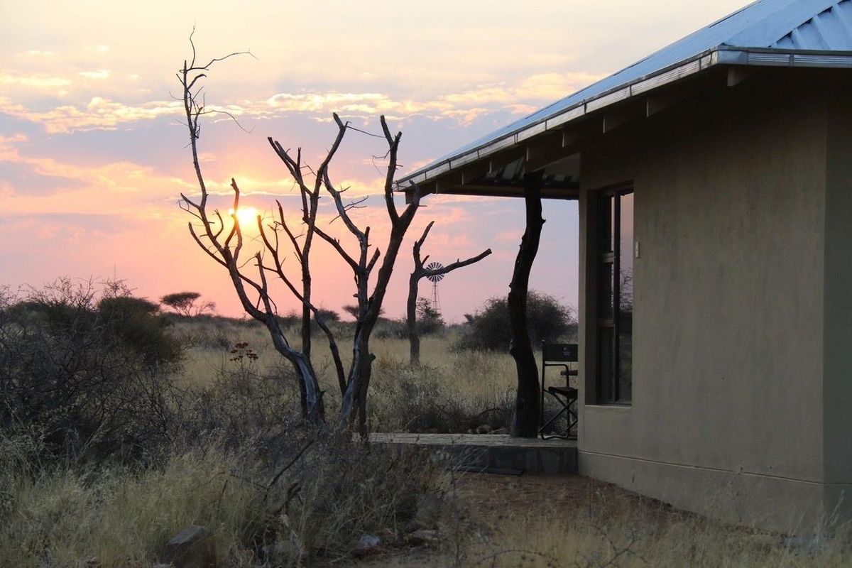 A serene view of a farm dwelling at sunset, featuring a covered patio area overlooking the natural landscape.