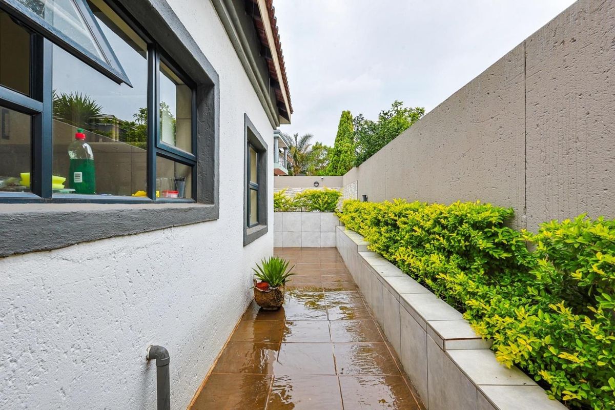 A narrow side exterior walkway featuring tiled flooring, a raised planter bed with established hedging, and a high boundary wall.