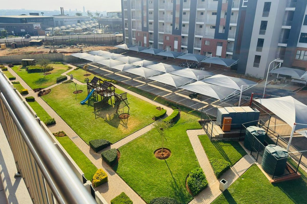 Elevated view of the apartment complex grounds featuring landscaped lawns, paved walkways, a children's play area, and covered parking bays.