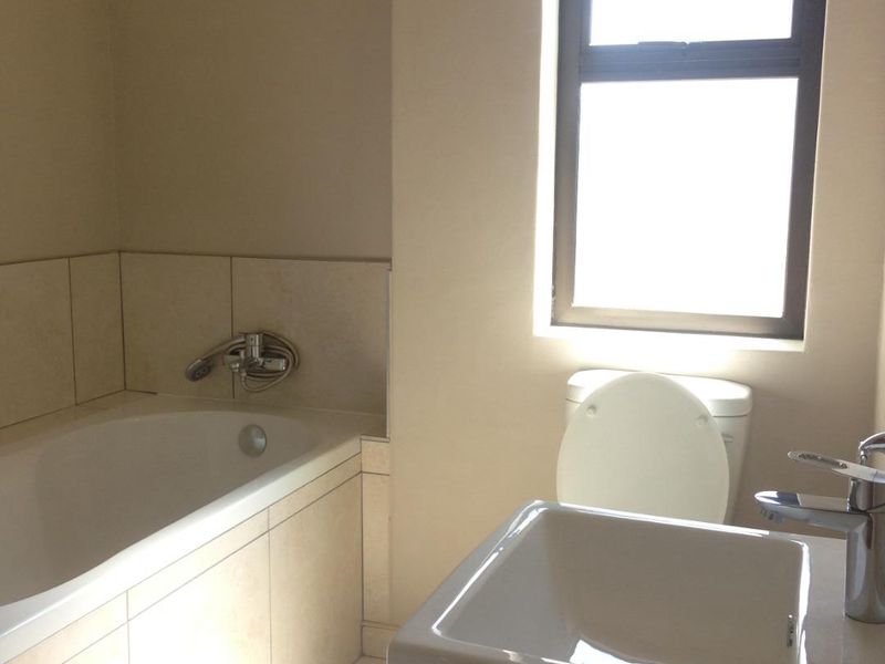 A clean, functional bathroom featuring a built-in bathtub with tiled surround, a modern wall-mounted basin, and a toilet.