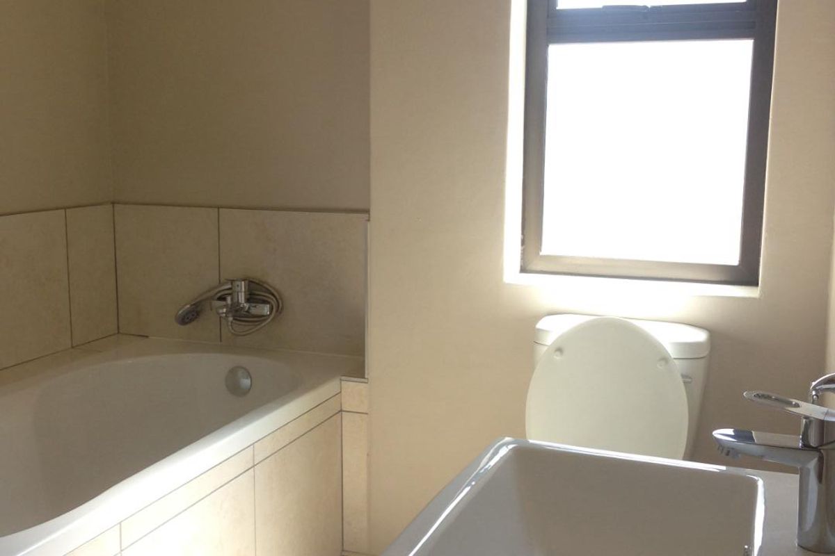 A clean, functional bathroom featuring a built-in bathtub with tiled surround, a modern wall-mounted basin, and a toilet.