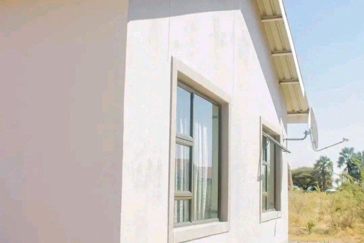 Side exterior view of the house featuring plastered walls, aluminium window frames, and a pitched roof with overhanging eaves.