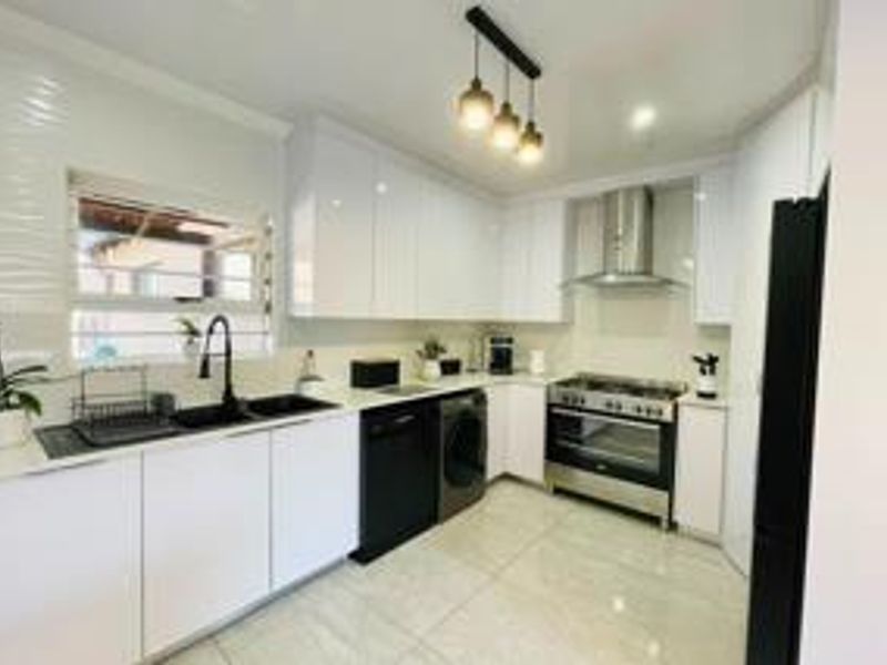 Modern kitchen featuring sleek white cabinetry, stainless steel gas stove with extractor fan, double sink, and contemporary pendant lighting.