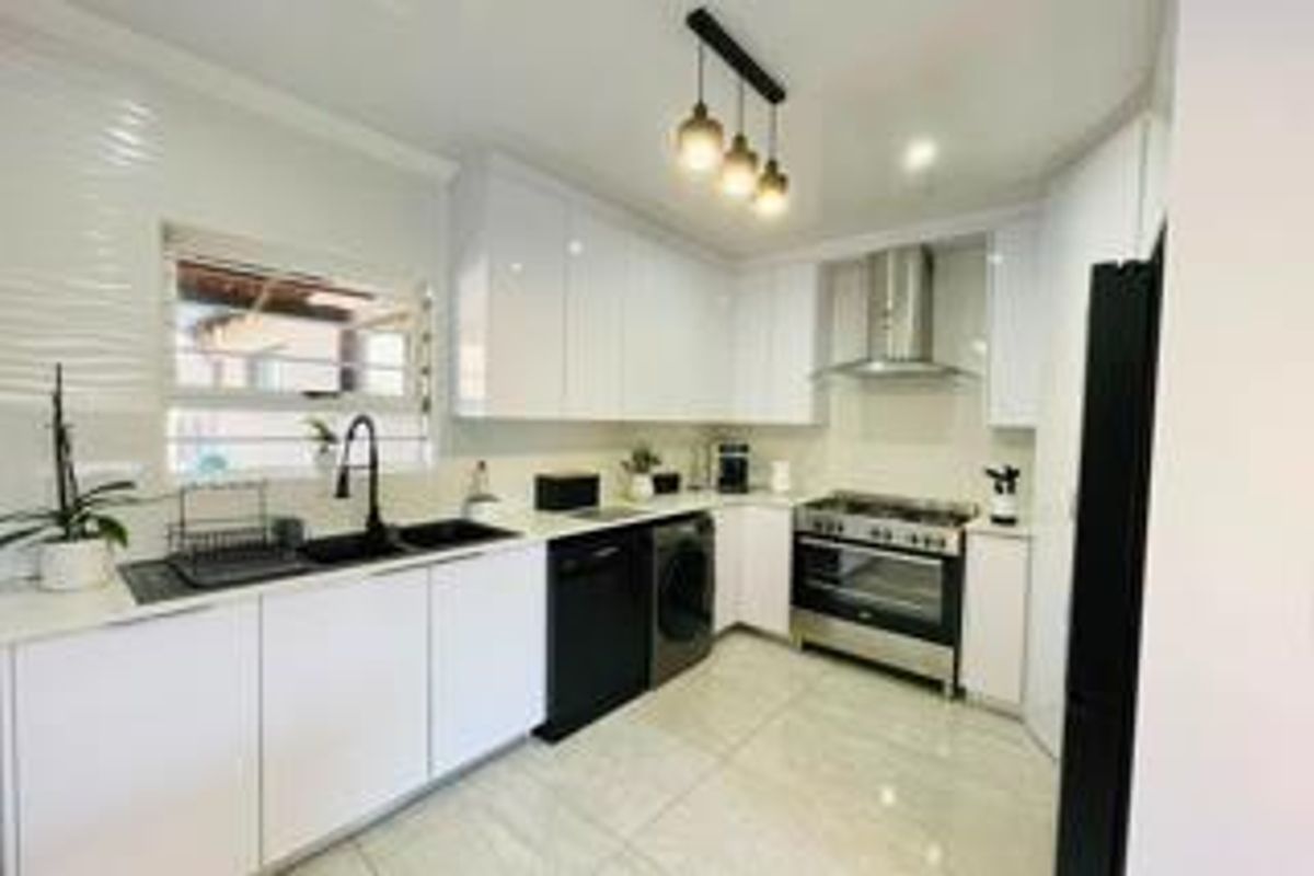 Modern kitchen featuring sleek white cabinetry, stainless steel gas stove with extractor fan, double sink, and contemporary pendant lighting.