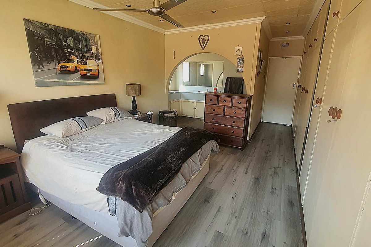 A bedroom featuring built-in cupboards, wood-look laminate flooring, a ceiling fan, and an arched opening leading to an en-suite vanity area.